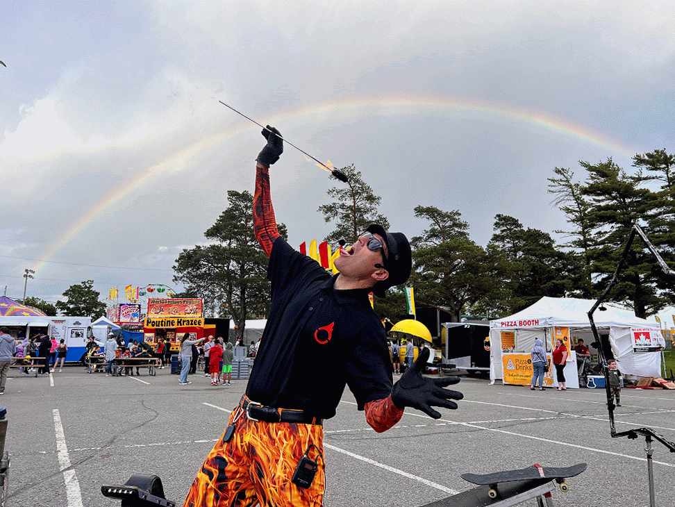 GIF of FireGuy eating fire under a rainbow at a fair.