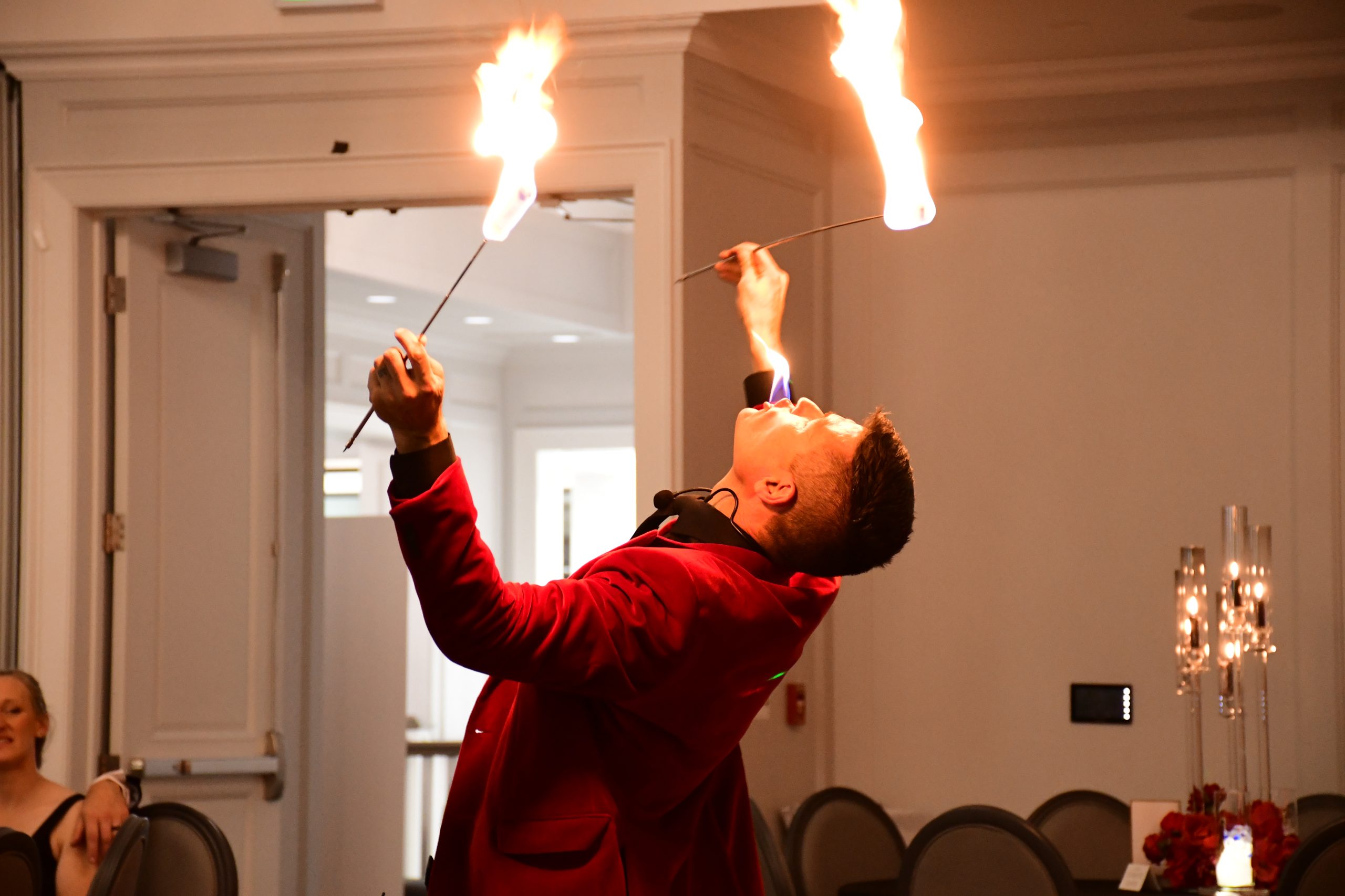 FireGuy eating fire while holding two fire sticks in his hands.